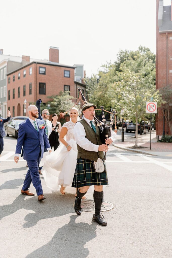 Couple walking in the street with bagpipe player after their wedding ceremony