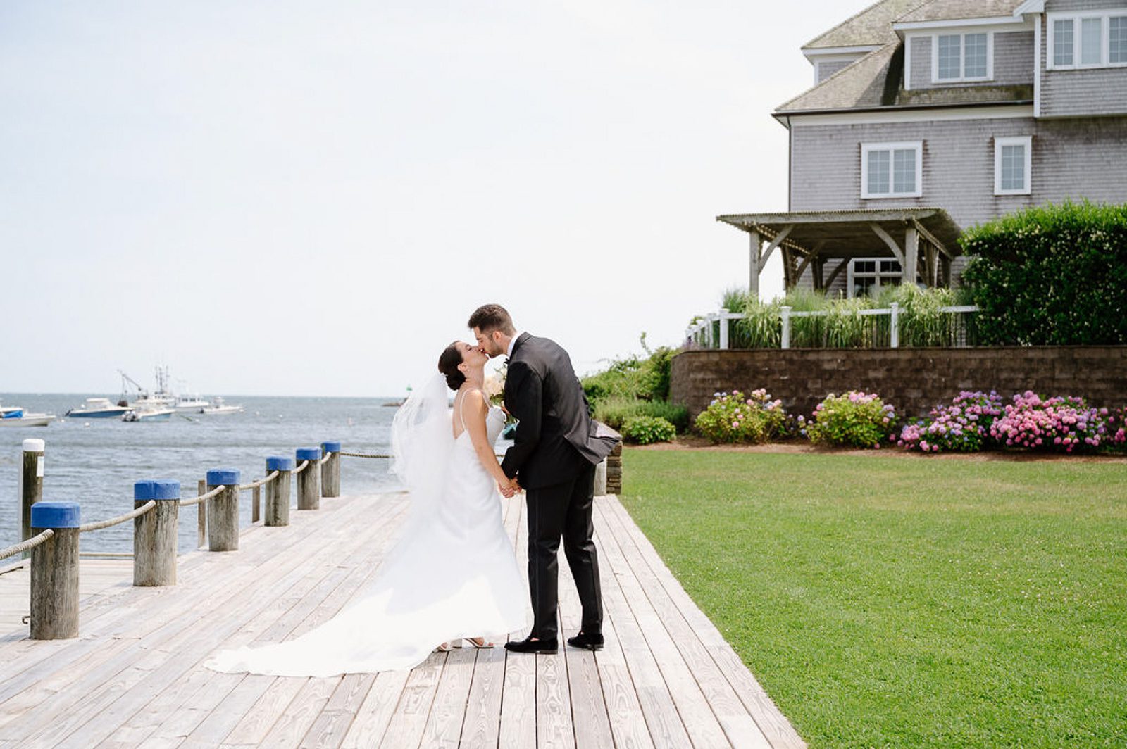 newlyweds kissing outside a New England beach house, planned as part of their wedding timeline. 