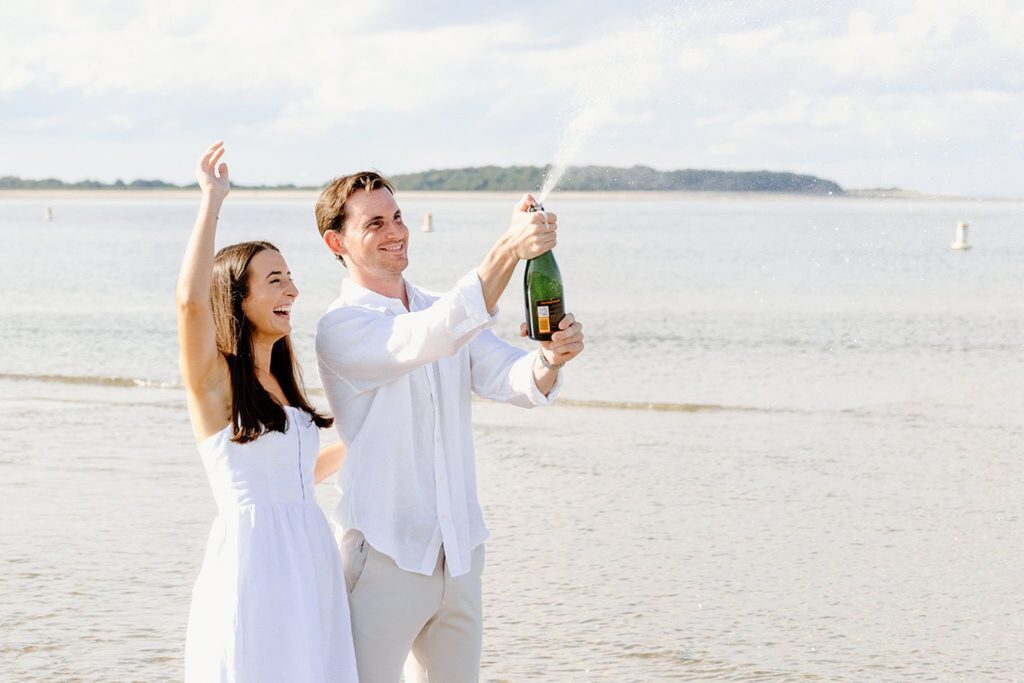 Popping Veuve champagne during beach engagement photos 