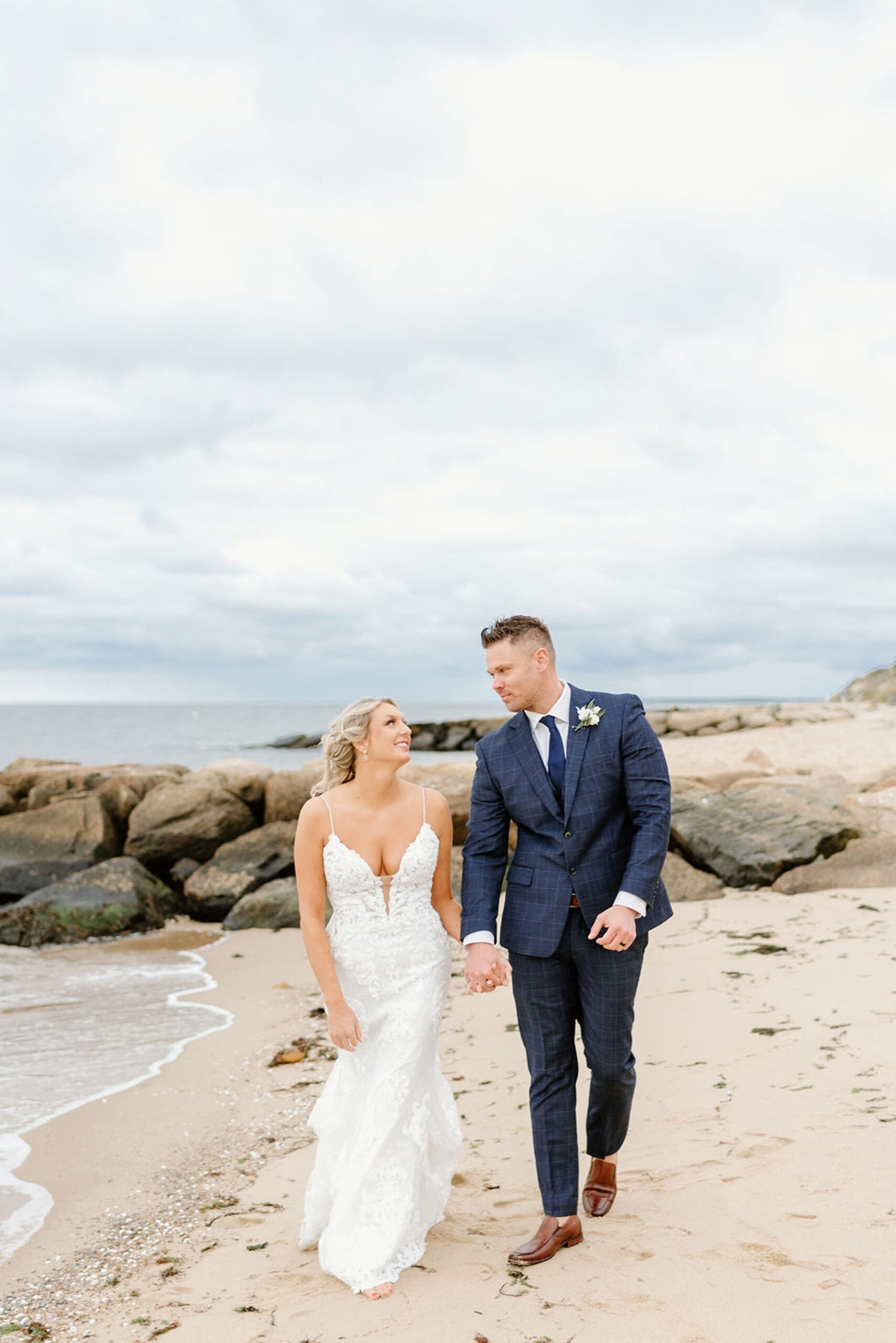 couple holding hands and walking on the beach at Oceanview of Nahant, one of the best small wedding venues in MA. 