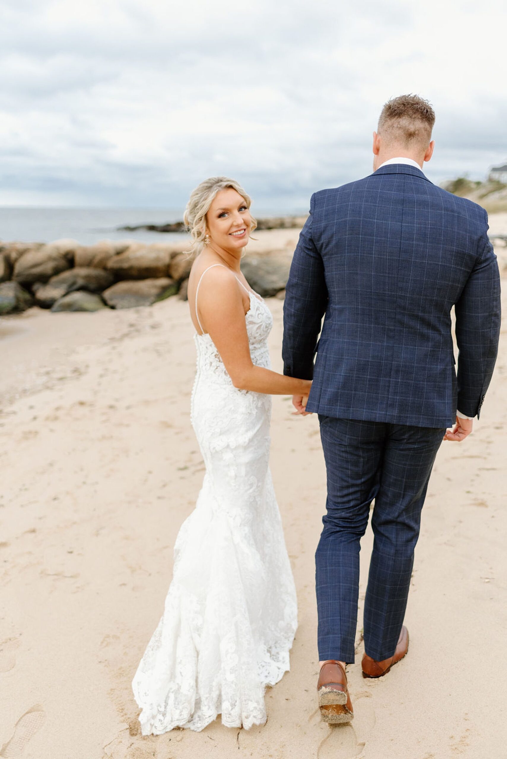 newlyweds holding hands and walking along the beach at Oceanview of Nahant, one of the best small wedding venues in MA. 