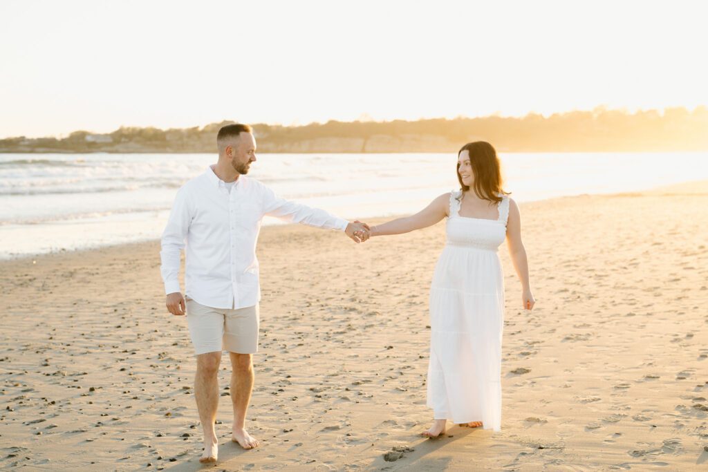 a couple holding hands at sunset on a new england beach comfortable in front of the camera. 