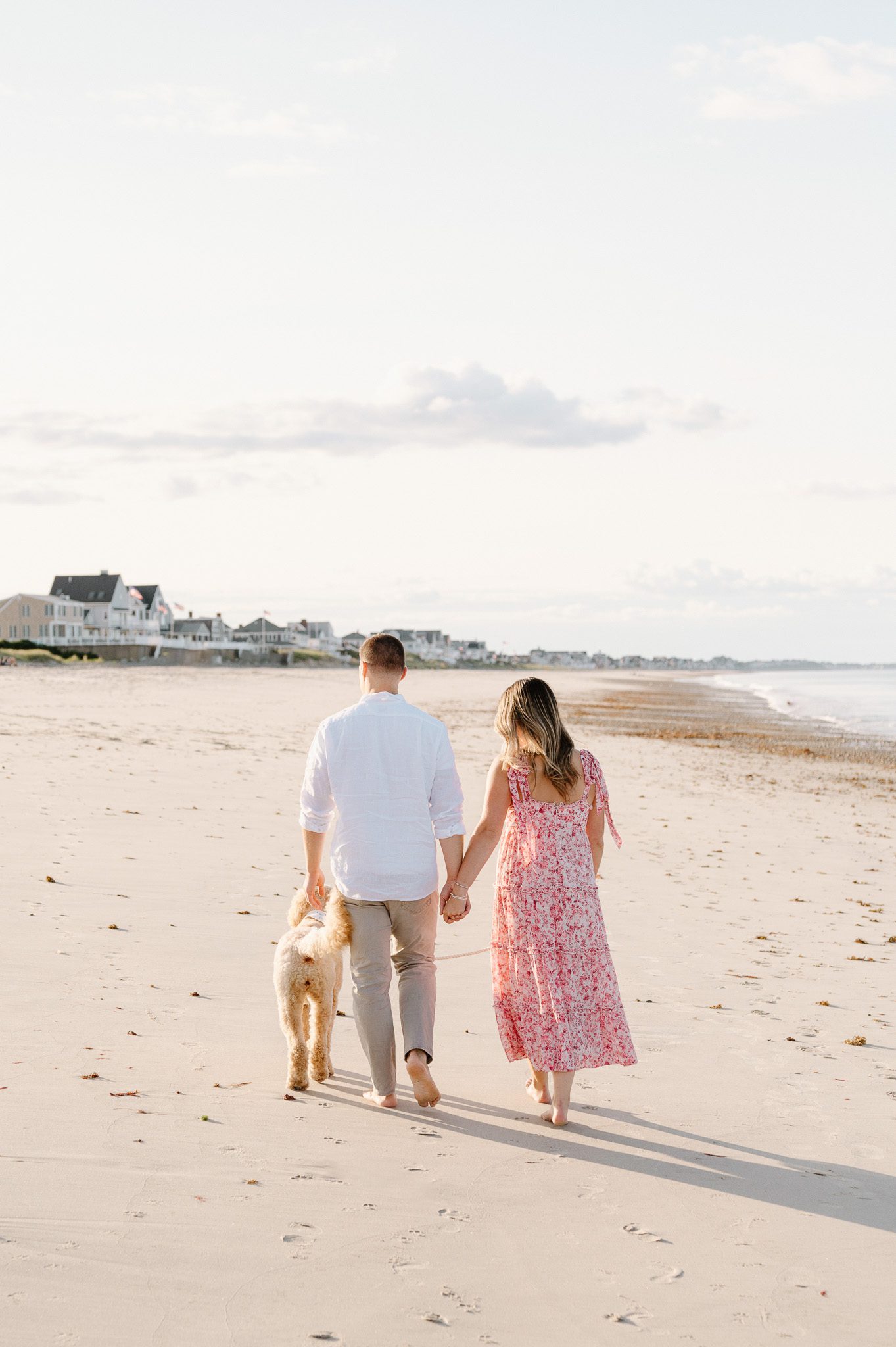 a couple walking with their dog on the sand. 