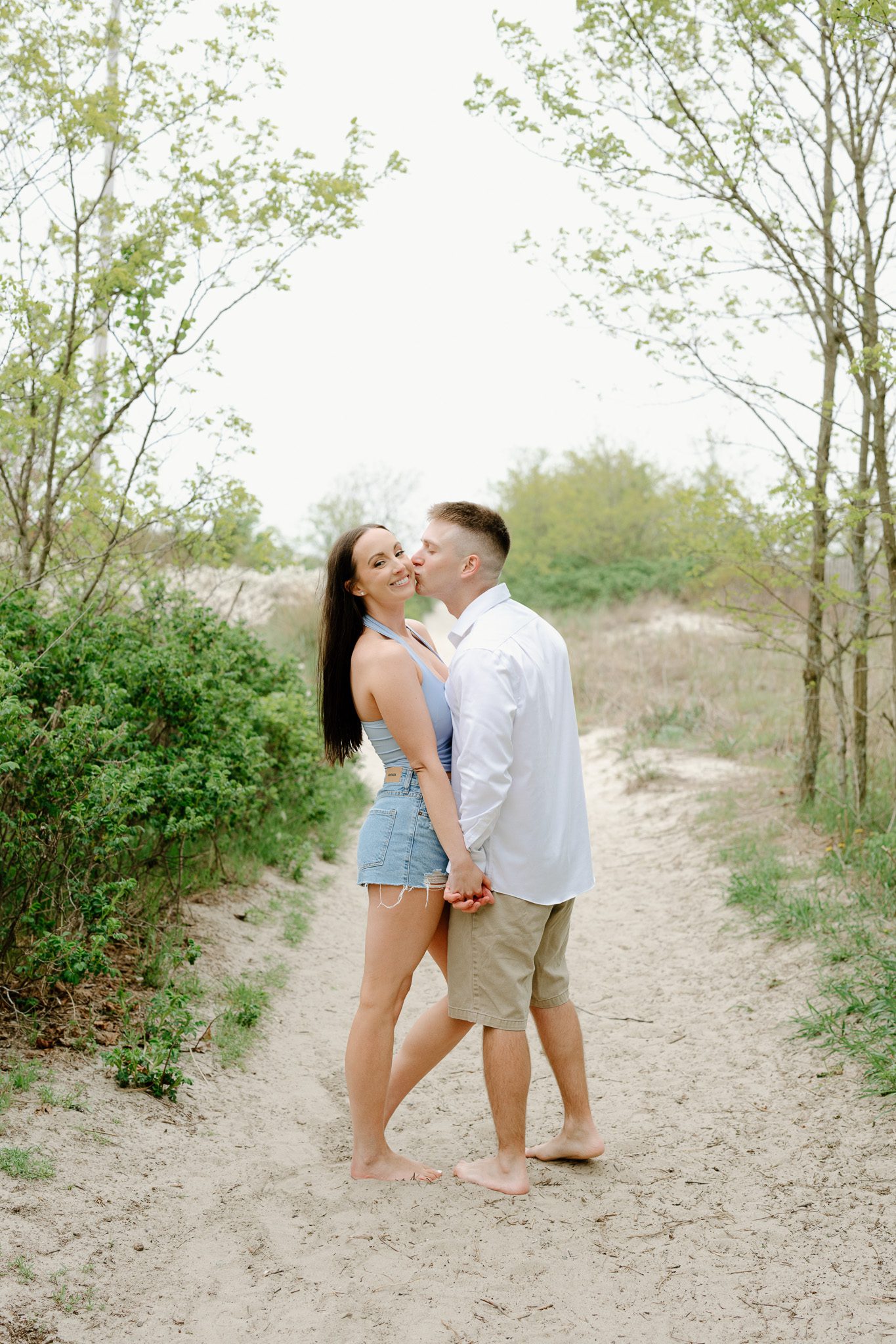 a couple kissing and holding hands on the beach, comfortable in front of the camera. 