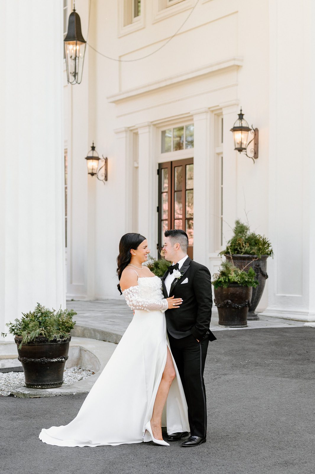 newlyweds posing in front of a white mansion as part of their wedding photography experience.