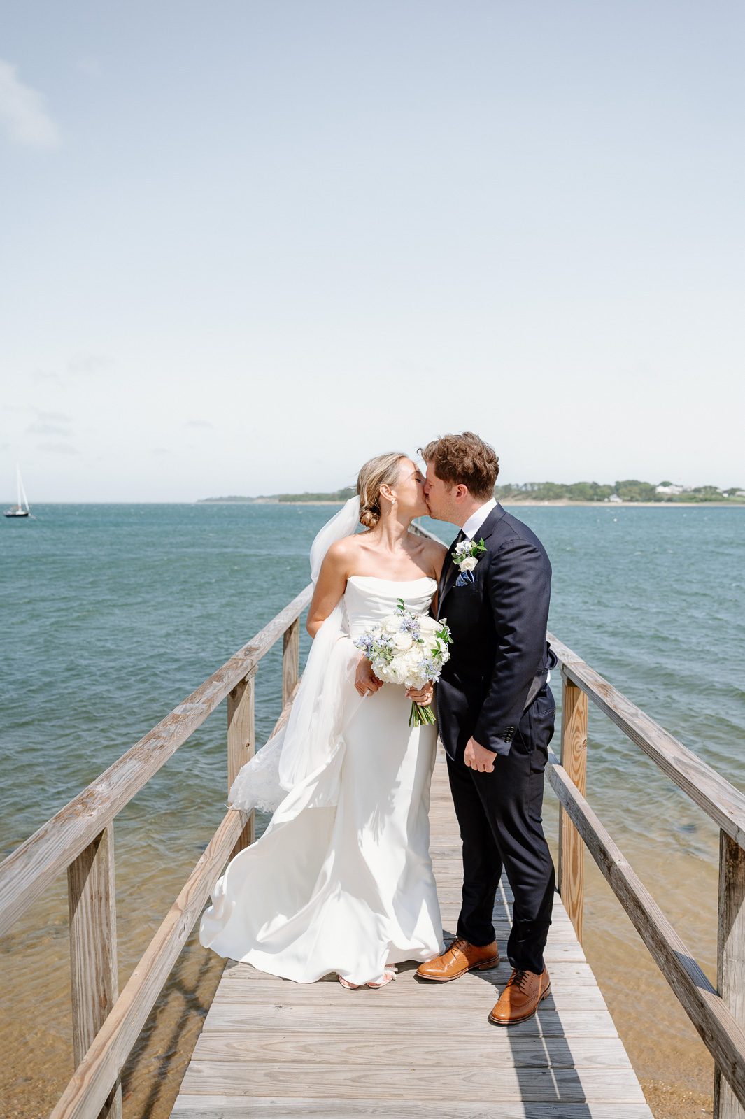 newlyweds kissing on a pier with the ocean around them.