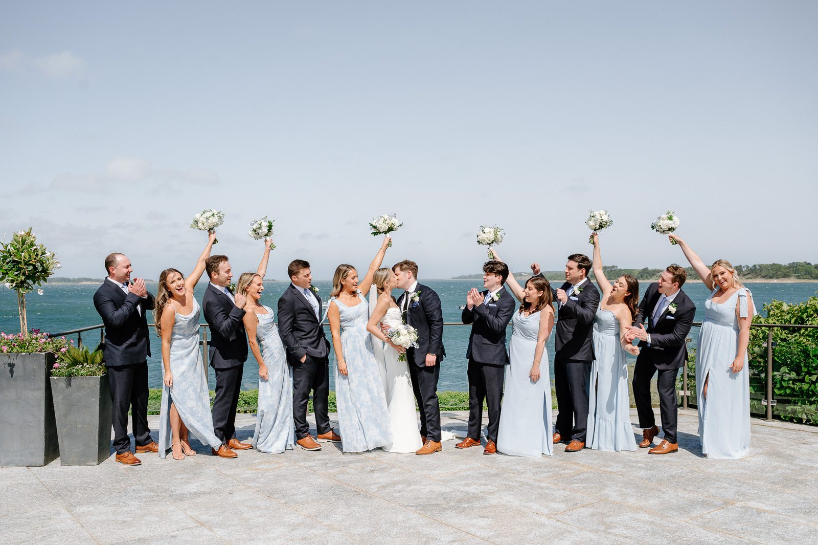 newlyweds kissing with their wedding party cheering, part of the wedding photography experience.