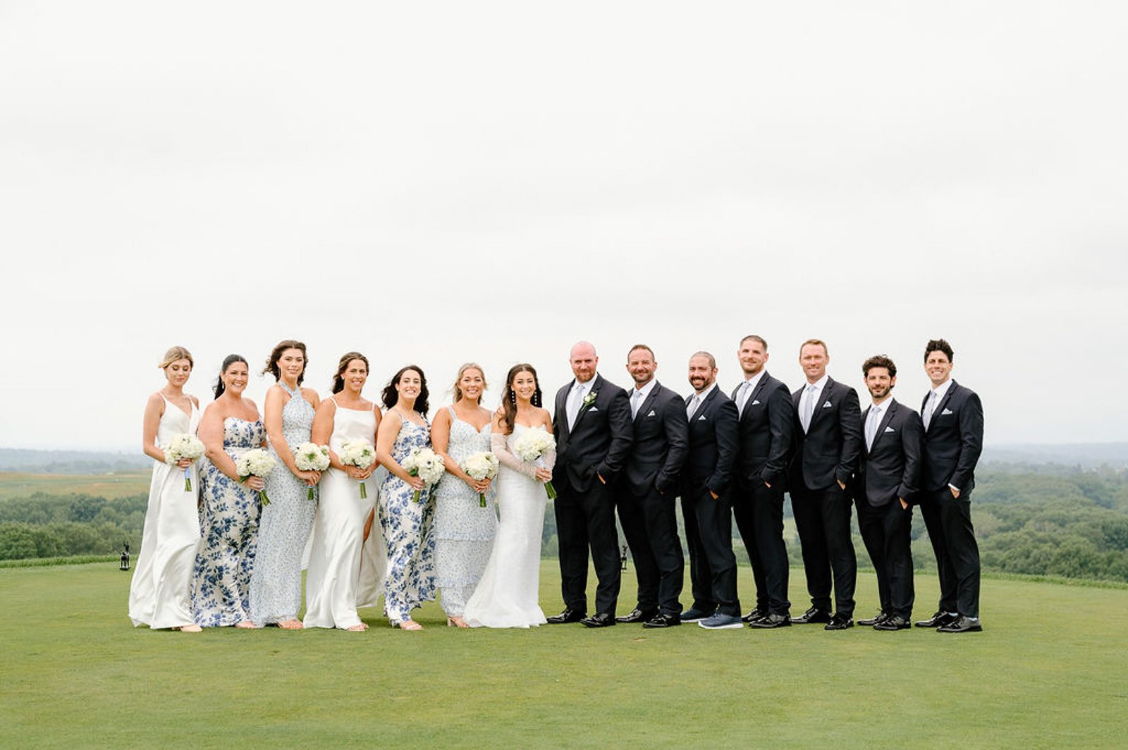 newlyweds and their wedding party posing on a grassy lawn. 