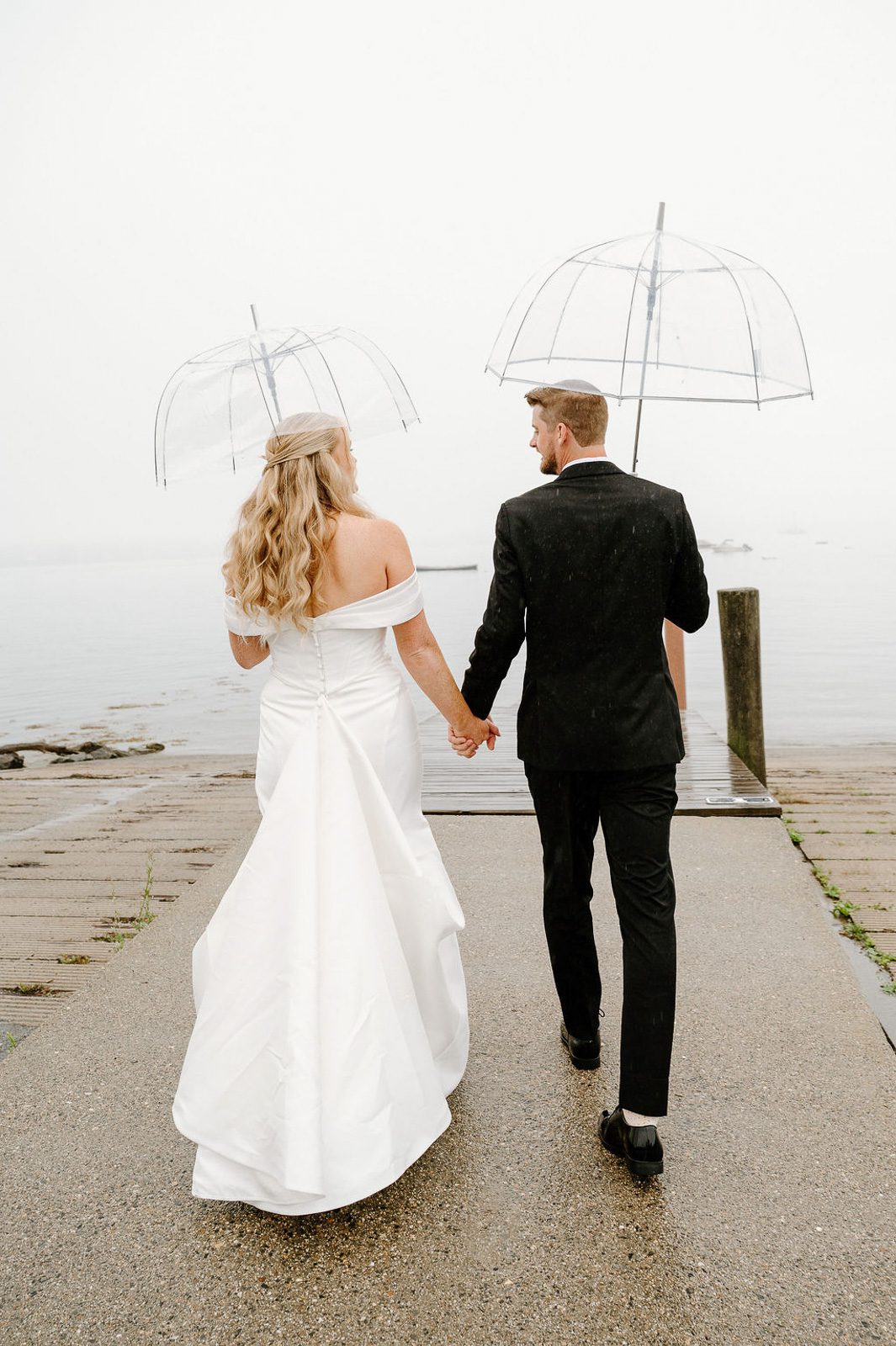 newlyweds holding hands under an umbrella, happy because they had a plan for when it rains on their wedding day. 