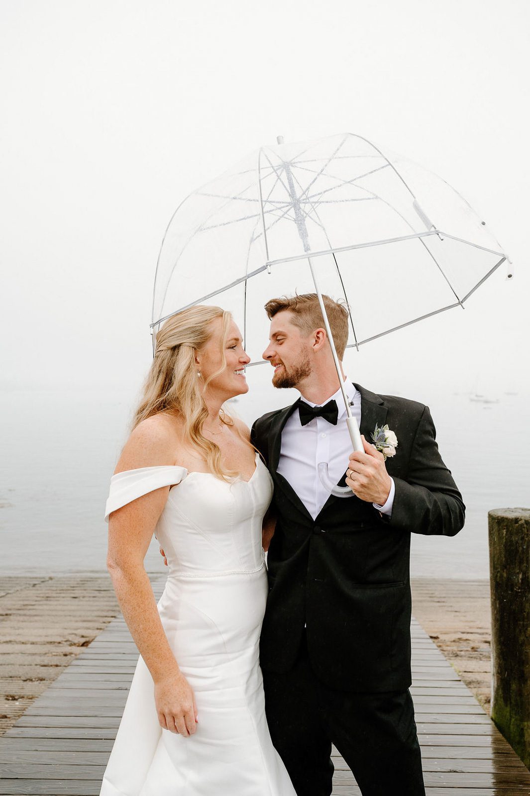 newlyweds hugging under an umbrella on a rainy boardwalk. 