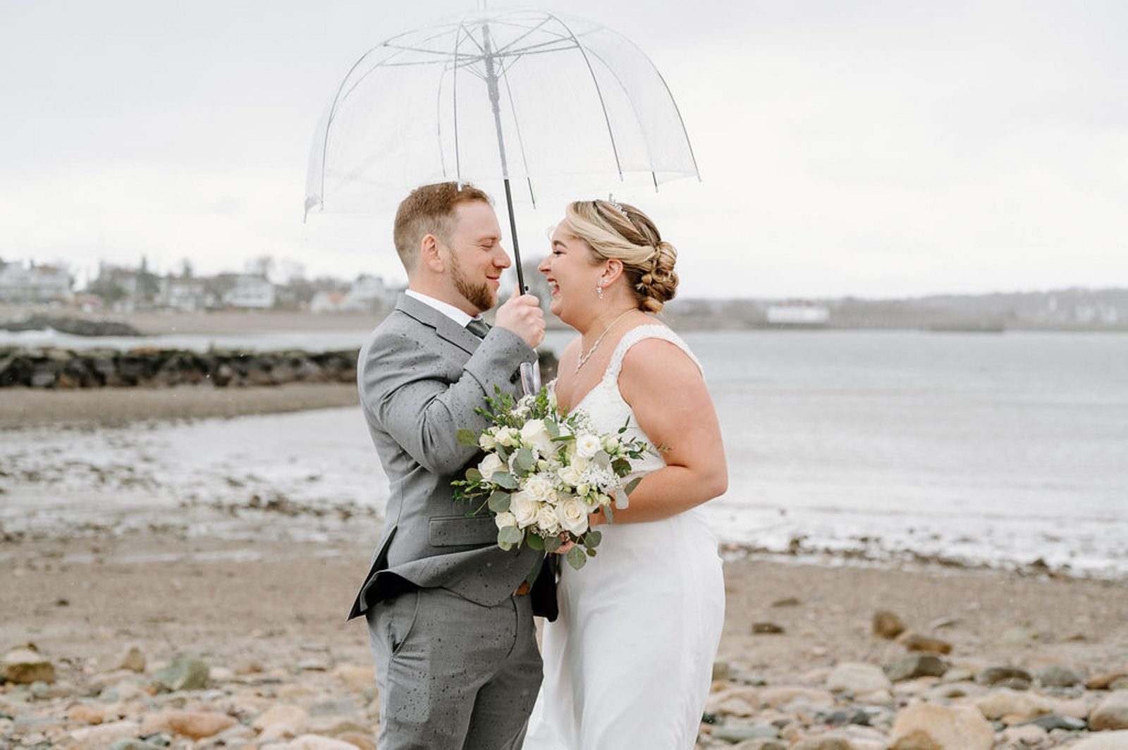 newlyweds standing under an umbrella, happy they had a plan for when it rains on their wedding day. 