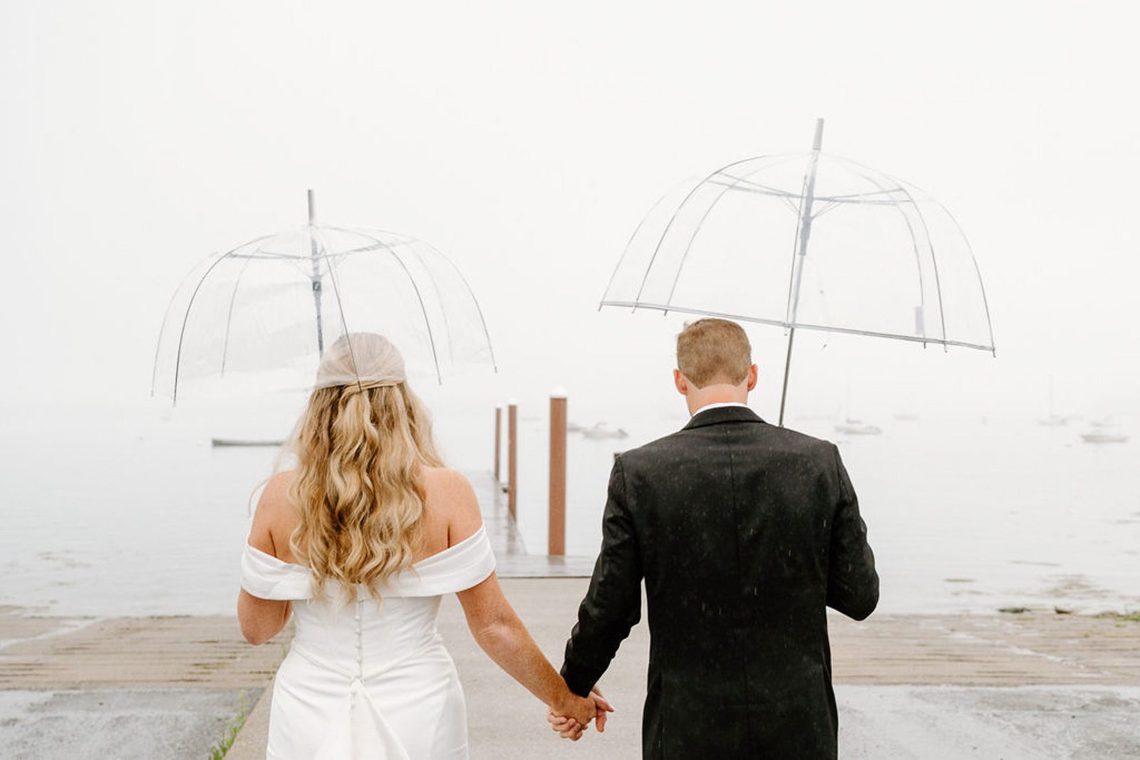 newlyweds walking in the rain with clear umbrellas. 