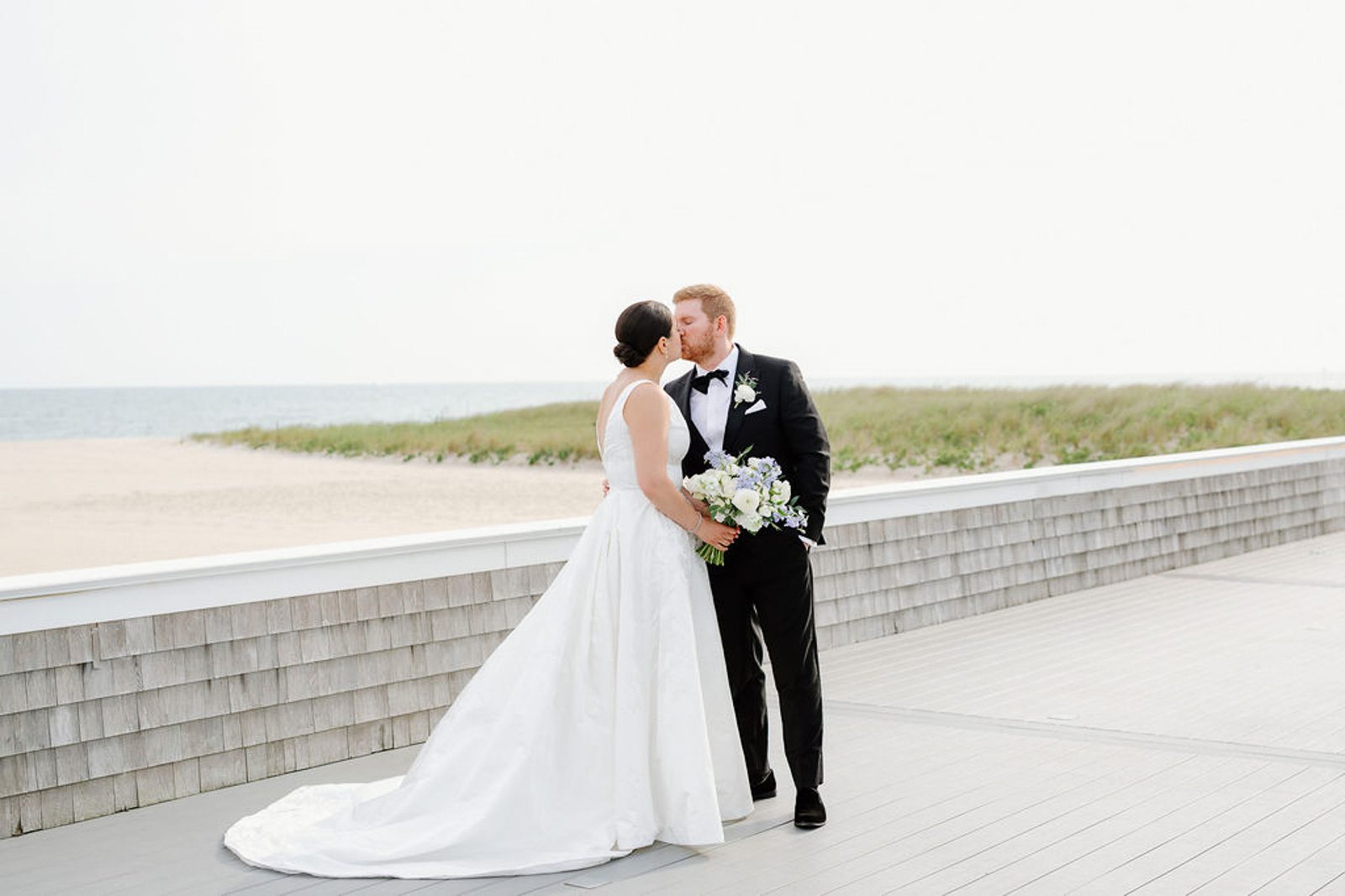 newlyweds kissing on a boardwalk with the ocean in the background, beautifully captured by their last minute wedding photographer. 