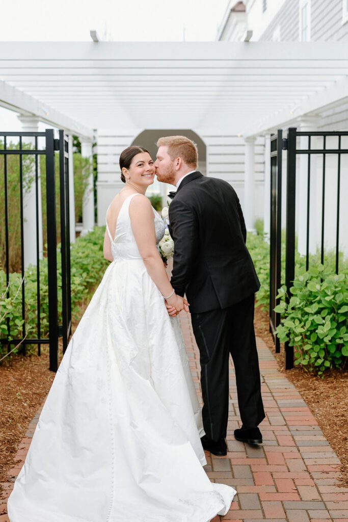 newlyweds kissing on a brick pathway under a pergola, beautifully captured by their last minute wedding photographer.