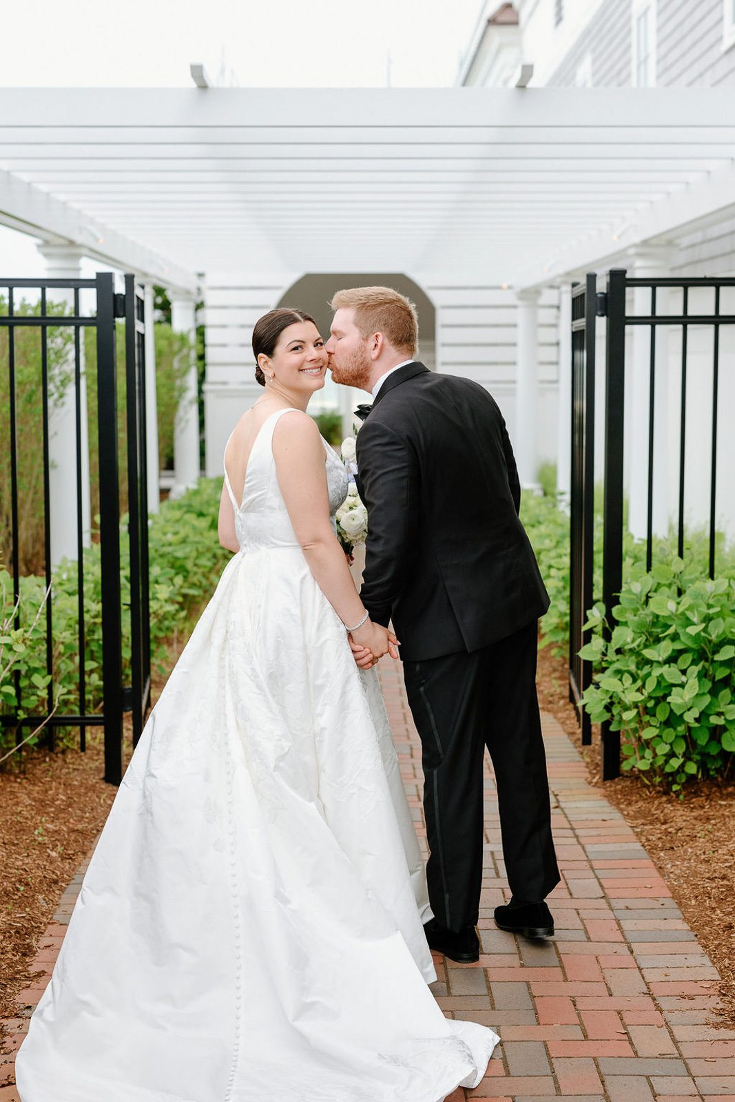 newlyweds kissing on a brick pathway under a pergola, beautifully captured by their last minute wedding photographer.