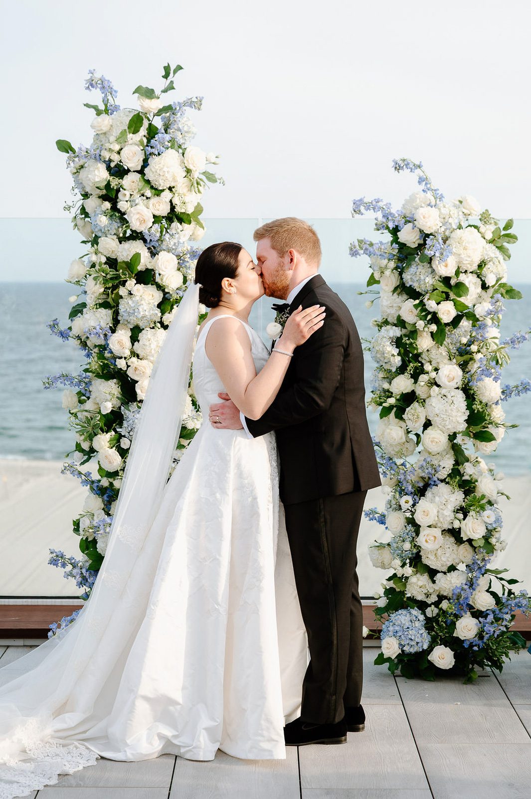 newlyweds kissing at the alter with floral columns and the ocean behind them. 