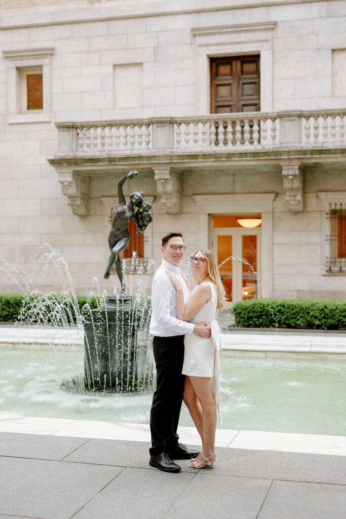 a couple hugging in front of a fountain at the Boston Public Library.