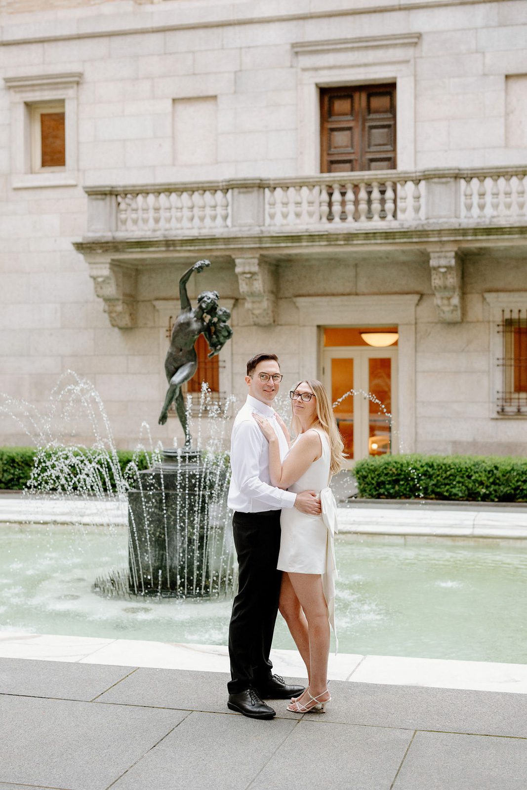 a couple hugging in front of a fountain at the Boston Public Library.